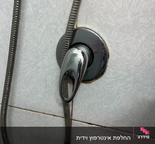 ברז כרום עם צינור מתכת על קיר אריחים